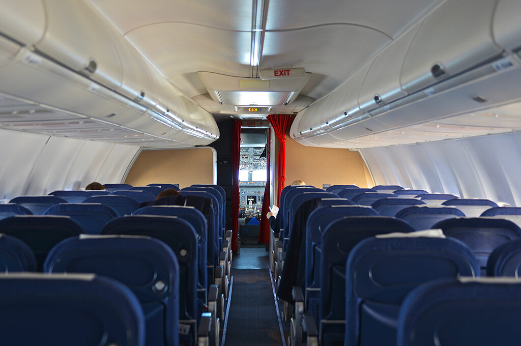 Looking down the aisle of an empty airplane cabin with blue seats and closed overhead compartments, setting the scene for what to do on a long haul flight.