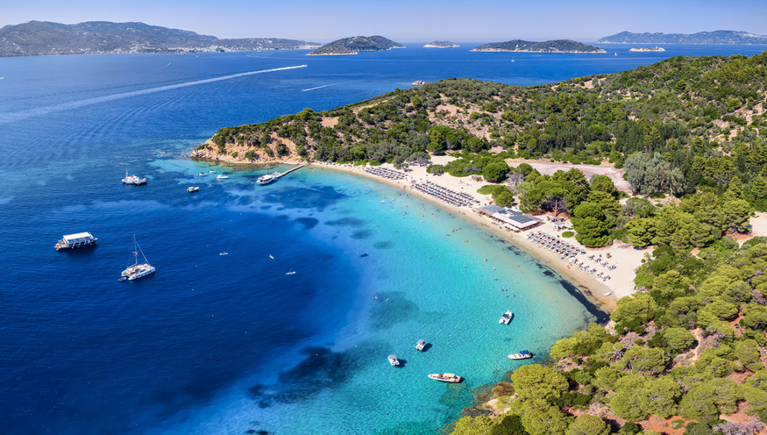 Aerial view of a turquoise beach cove with boats and lush green pine trees, one of the most popular holiday destinations in the Mediterranean.