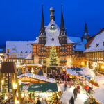 snowy evening view of a festive market square showcasing one of the best European Christmas markets with timber-framed stalls and a glowing tree.