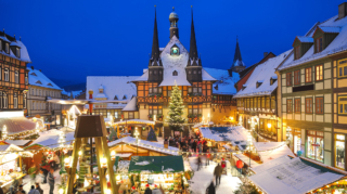 snowy evening view of a festive market square showcasing one of the best European Christmas markets with timber-framed stalls and a glowing tree.