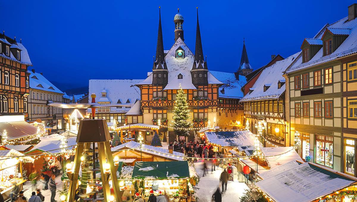 snowy evening view of a festive market square showcasing one of the best European Christmas markets with timber-framed stalls and a glowing tree.