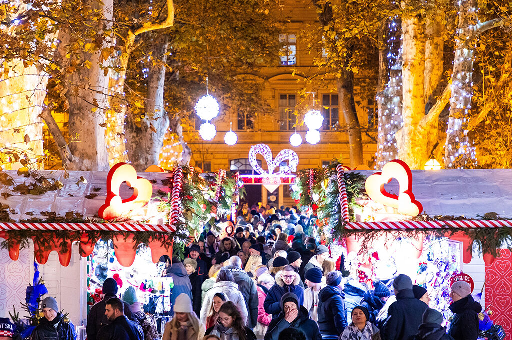 A bustling winter walkway illuminated by hanging lights and heart-shaped holiday decorations at one of the best European Christmas markets.