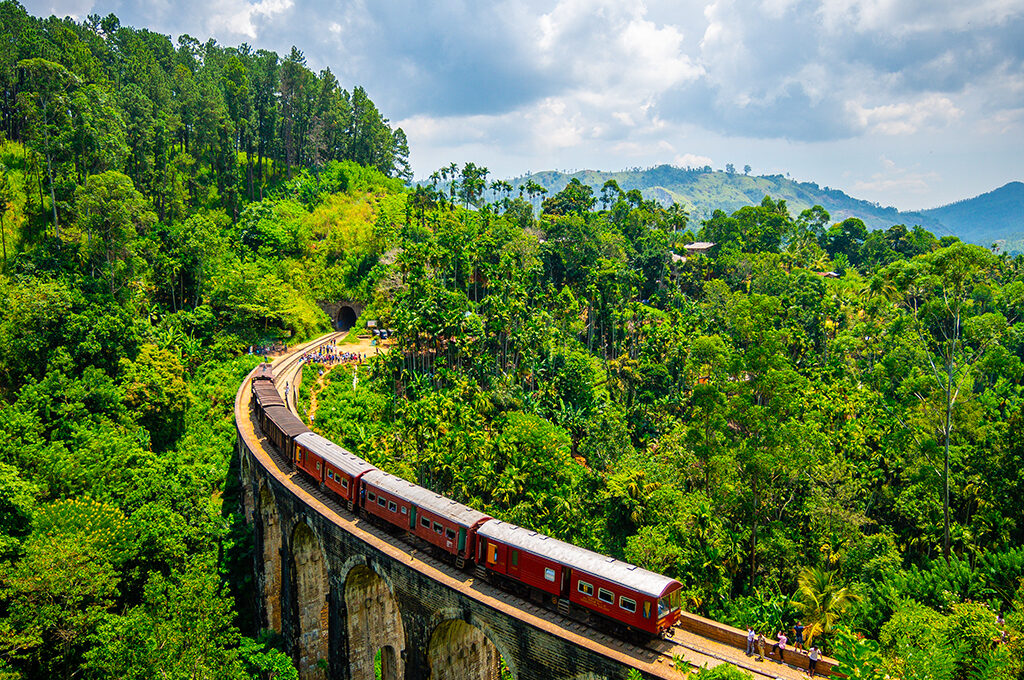 Historic train crossing a stone viaduct bridge surrounded by lush green tropical jungle and mountains in Sri Lanka is one of the most popular holiday destinations.