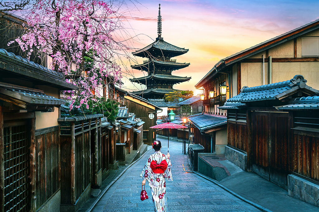A person wearing a traditional kimono walking down a historic cobblestone street lined with wooden buildings and cherry blossoms under a sunset sky in Japan is one of the most popular holiday destinations.