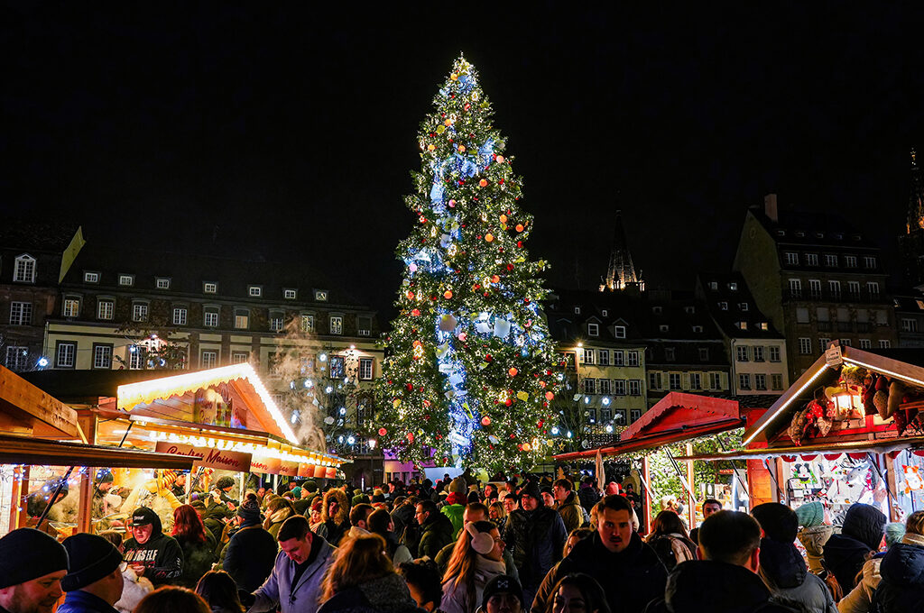 A crowded plaza featuring a massive lit Christmas tree, highlighting a vibrant atmosphere at one of the best European Christmas markets.