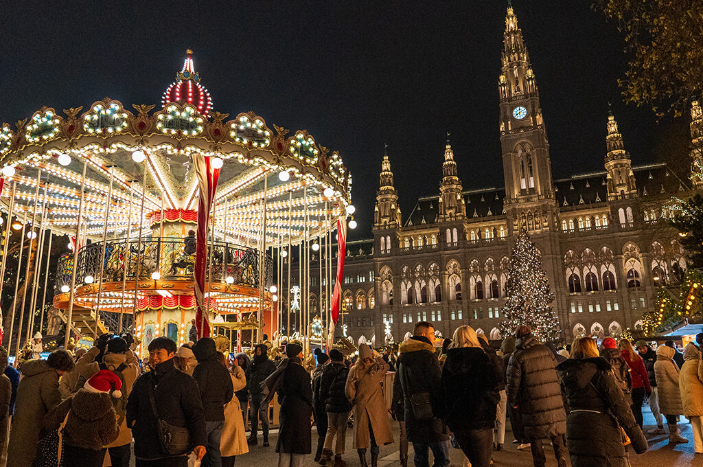 Visitors enjoying a brightly lit vintage carousel in front of a grand illuminated building at one of the best European Christmas markets.