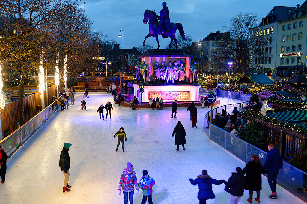 People ice skating on an outdoor rink surrounded by historic architecture and holiday lights at one of the best European Christmas markets.