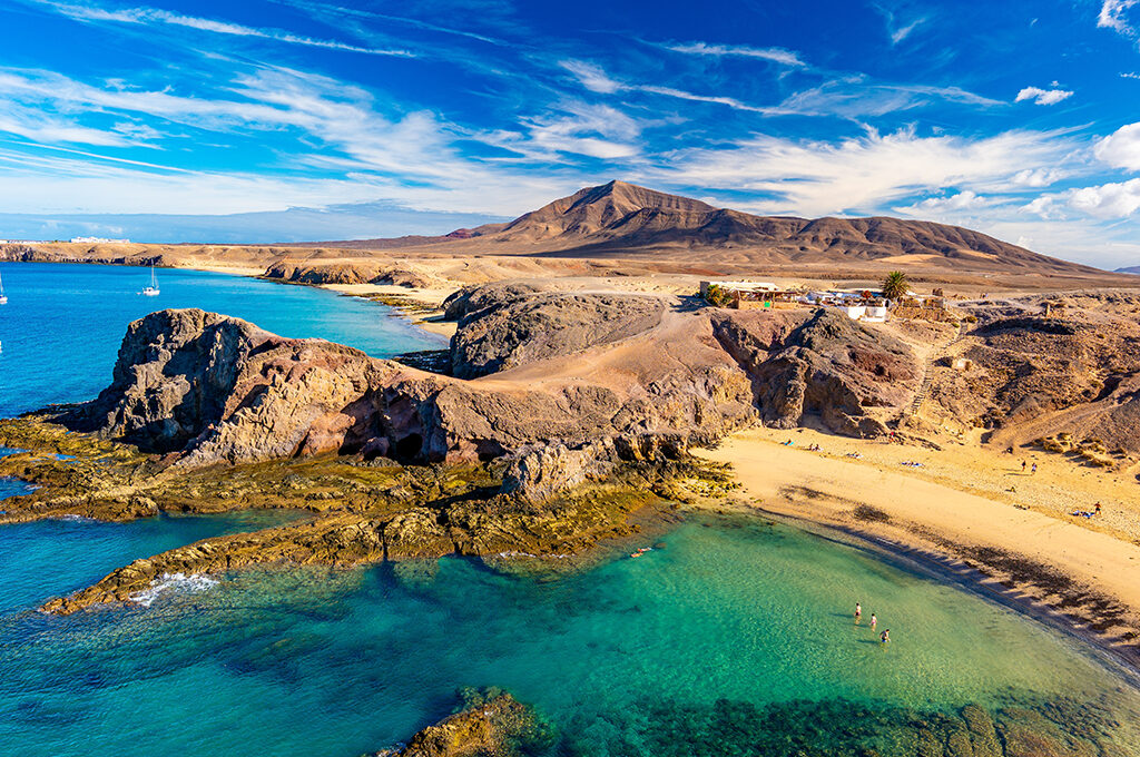 Beautiful coastal landscape with rugged cliffs, a sandy beach, and clear blue water, characteristic of the most popular holiday destinations.