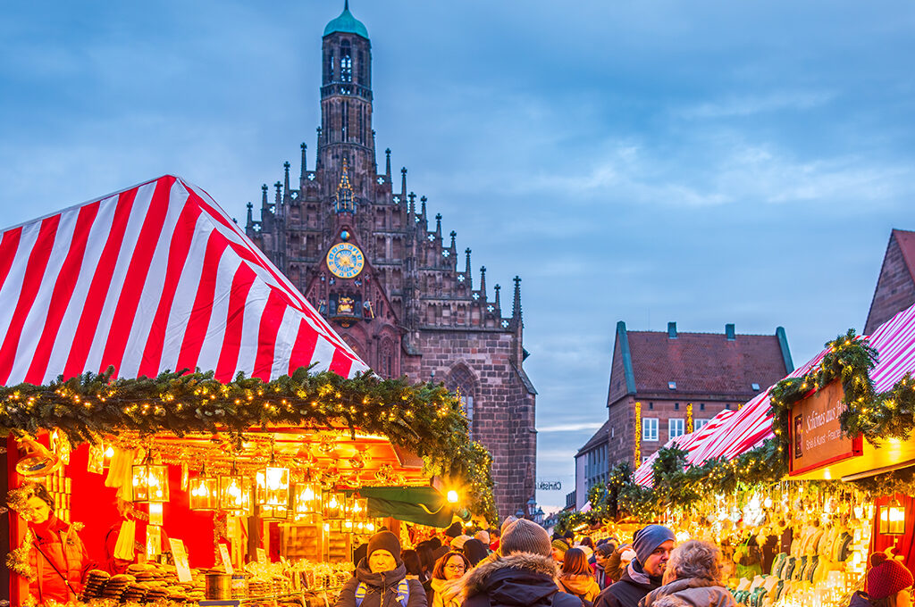 Traditional red-and-white striped market stalls adorned with pine garlands beneath a historic gothic tower, representing one of the best european christmas markets.
