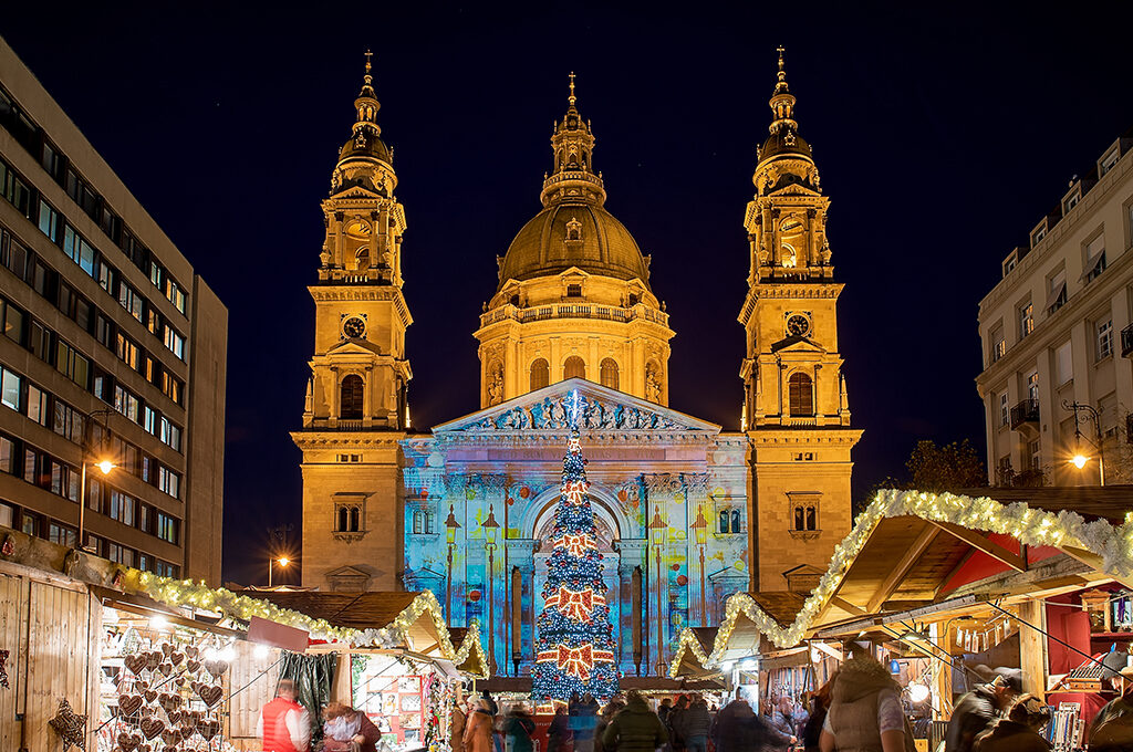 A brightly lit Christmas tree standing in front of a majestic illuminated cathedral at one of the best european christmas markets.