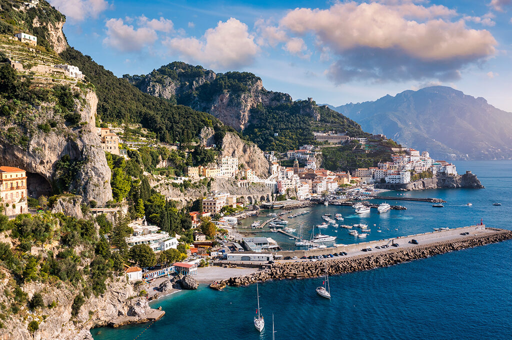 Coastal town nestled into steep mountain cliffs beside a harbor filled with boats, making it one of the most popular holiday destinations.