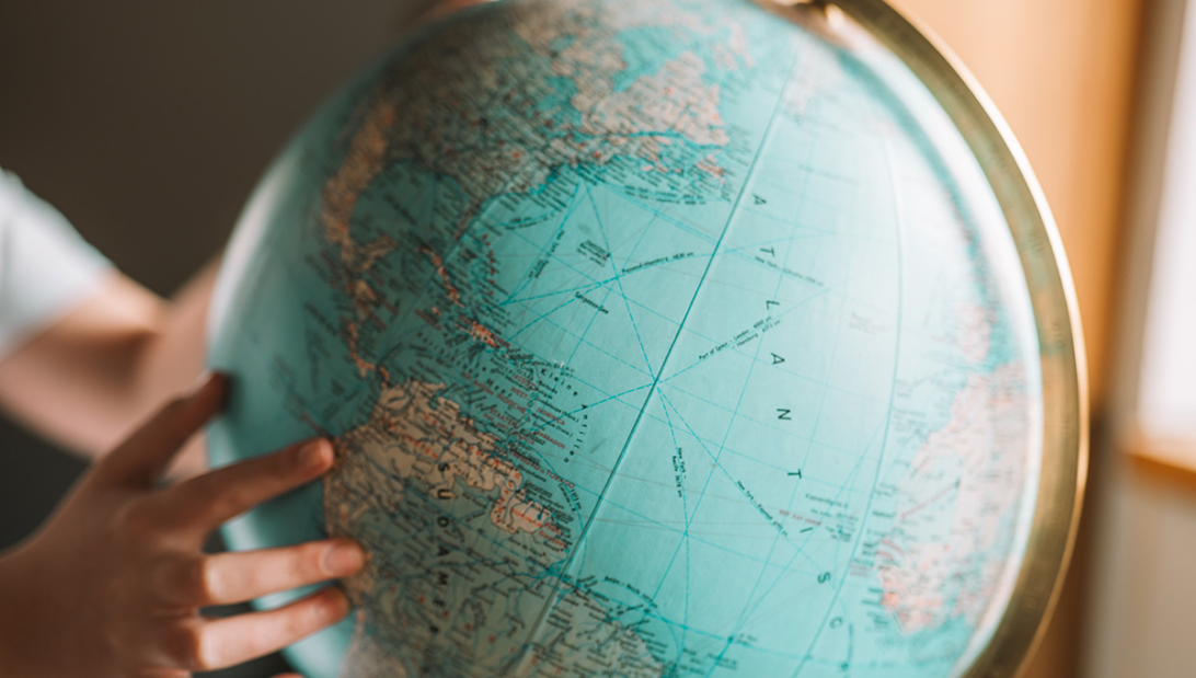 Person pointing at a world globe while researching the best time to book long haul flights.