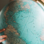 Person pointing at a world globe while researching the best time to book long haul flights.