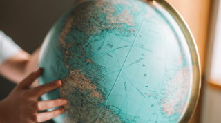 Person pointing at a world globe while researching the best time to book long haul flights.