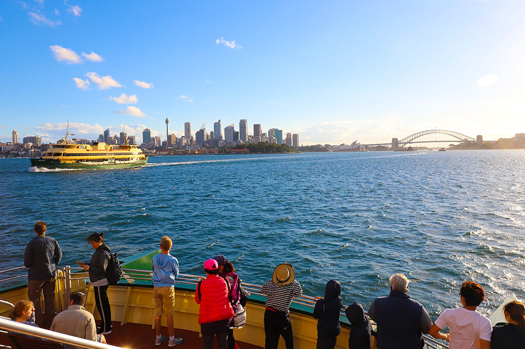 Photo of a group of people standing in the ferry looking at Opera House and Harbour Bridge