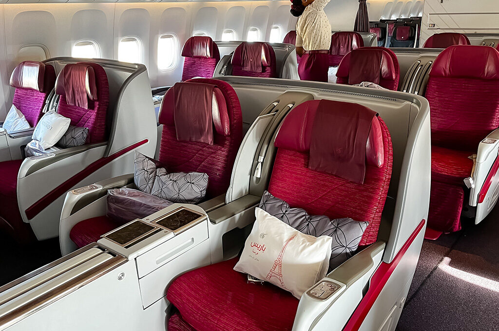 Empty business class airplane cabin featuring plush red seats and a white pillow with Paris written on it.