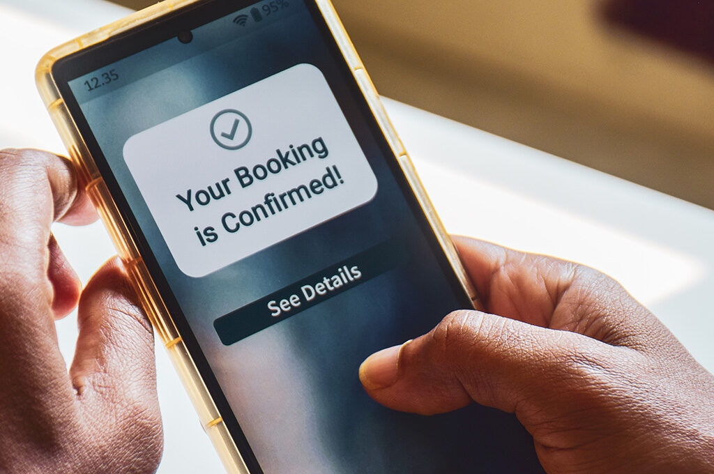 Close-up of hands holding a smartphone displaying a Your Booking is Confirmed notification.