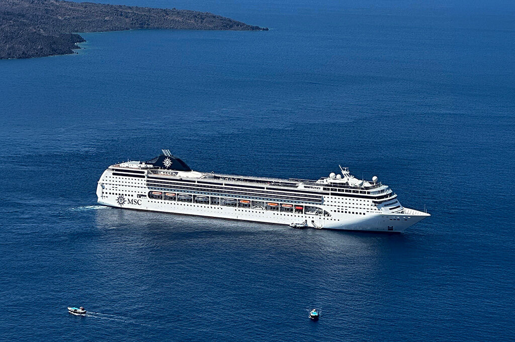 An aerial view of a cruise ship navigating calm blue sea water near a coastal shore.