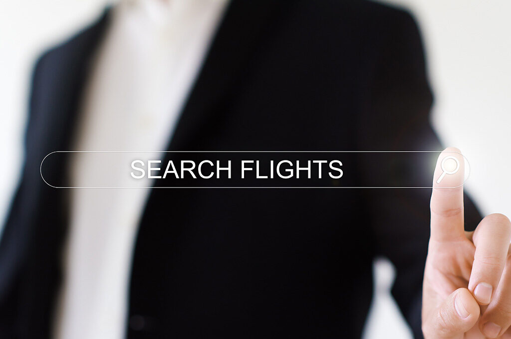 Person in a suit tapping a digital search flights button to find the best time to book long haul flights.