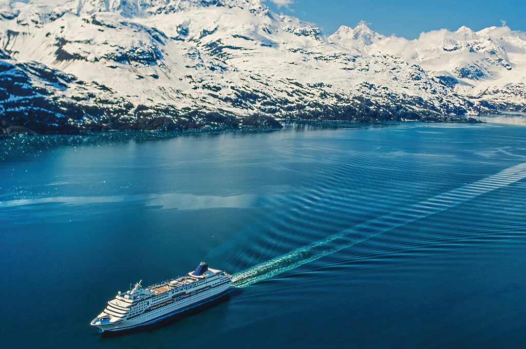 A cruise ship sailing through a majestic blue fjord surrounded by snow-capped mountains.