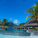 Infinity pool surrounded by palm trees and thatched-roof pavilions with mountain views at one of the best hotels in mauritius.