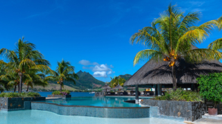 Infinity pool surrounded by palm trees and thatched-roof pavilions with mountain views at one of the best hotels in mauritius.