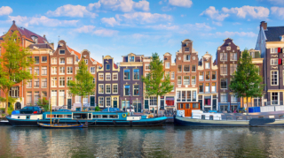 Amsterdam canal waterfront with colorful historic buildings and moored boats - quintessential places to visit in Netherlands with family for cultural exploration.