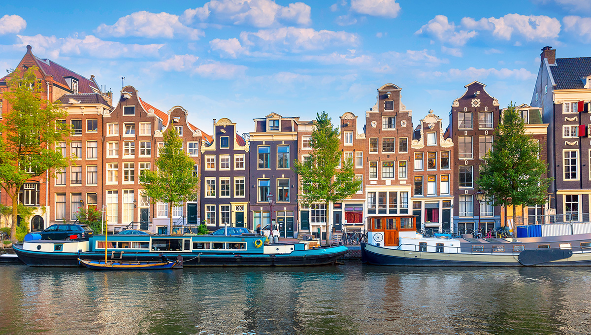 Amsterdam canal waterfront with colorful historic buildings and moored boats - quintessential places to visit in Netherlands with family for cultural exploration.