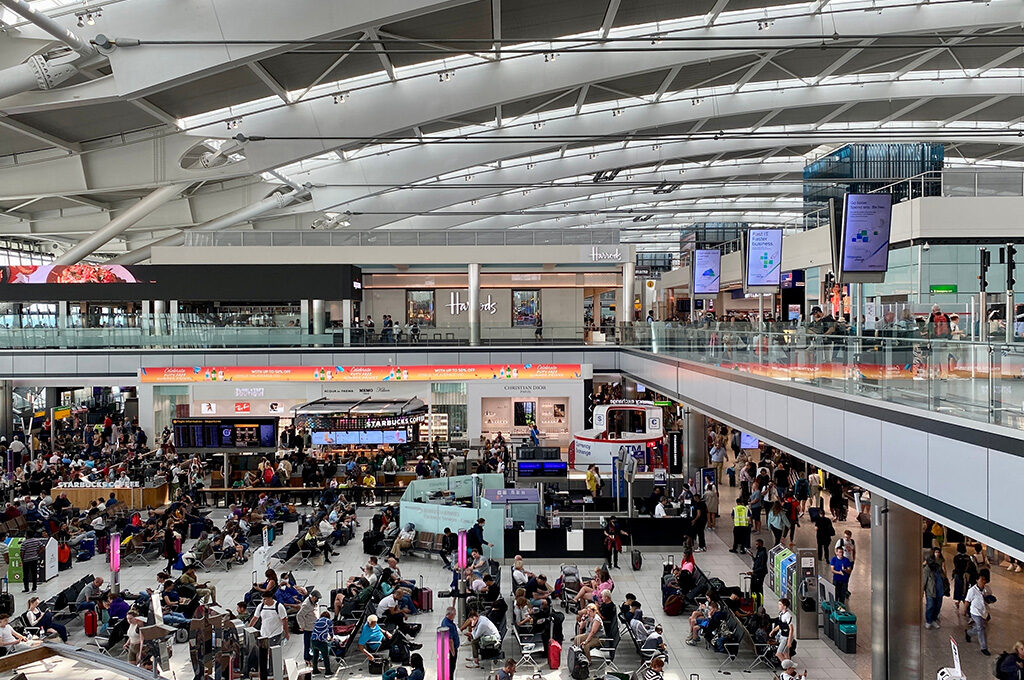 Interior view of London Heathrow Airport departure hall, consistently ranked among the busiest airports in Europe, showing passenger seating, Pret A Manger, and British Airways planes visible on the tarmac.