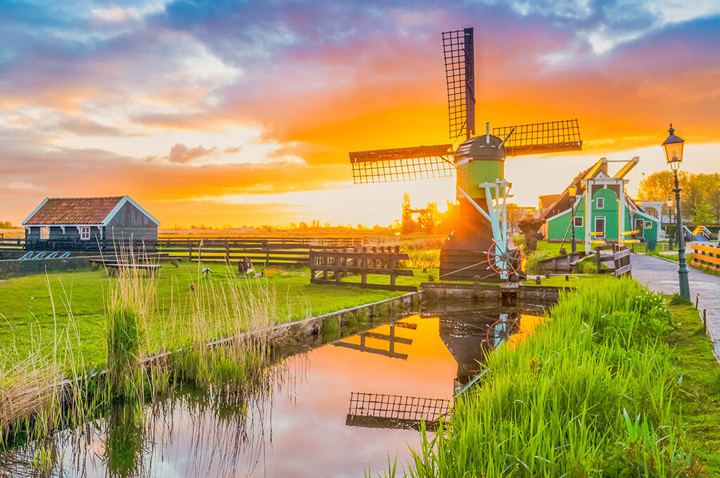 Traditional Dutch windmill reflected in water at sunset near Zaanse Schans - picturesque places to visit in Netherlands with family in the countryside villages.